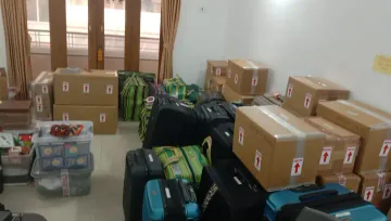 Packed cartons, luggage and bags grouped in a room.