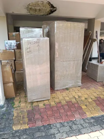 Wrapped tall household pieces and cartons gathered outside a building entrance.