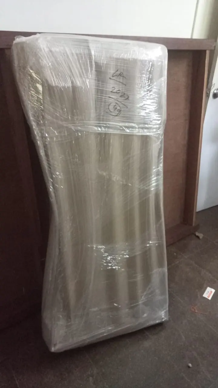An upright refrigerator covered in protective wrapping inside a room.