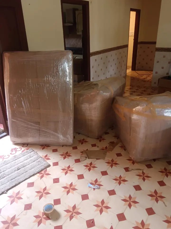 A broad wrapped furniture piece and smaller rounded packages standing in a room.