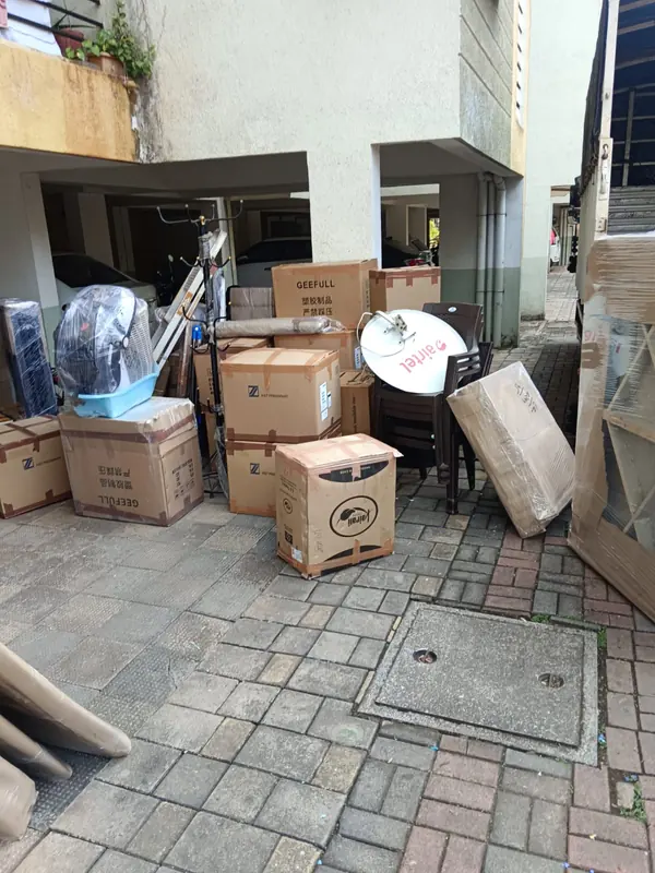 Packed cartons and assorted household pieces grouped outside a building entrance.