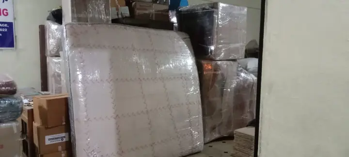 A broad flat furniture piece wrapped in protective material beside other packed goods.