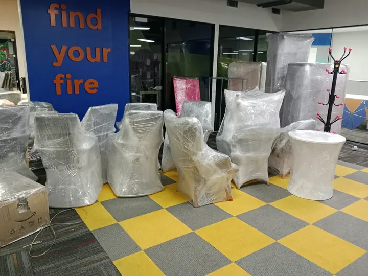 Wrapped chairs and taller furniture pieces grouped on a tiled floor.