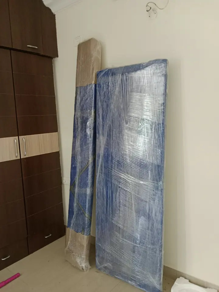 A tall flat furniture panel wrapped and standing beside an indoor wall.