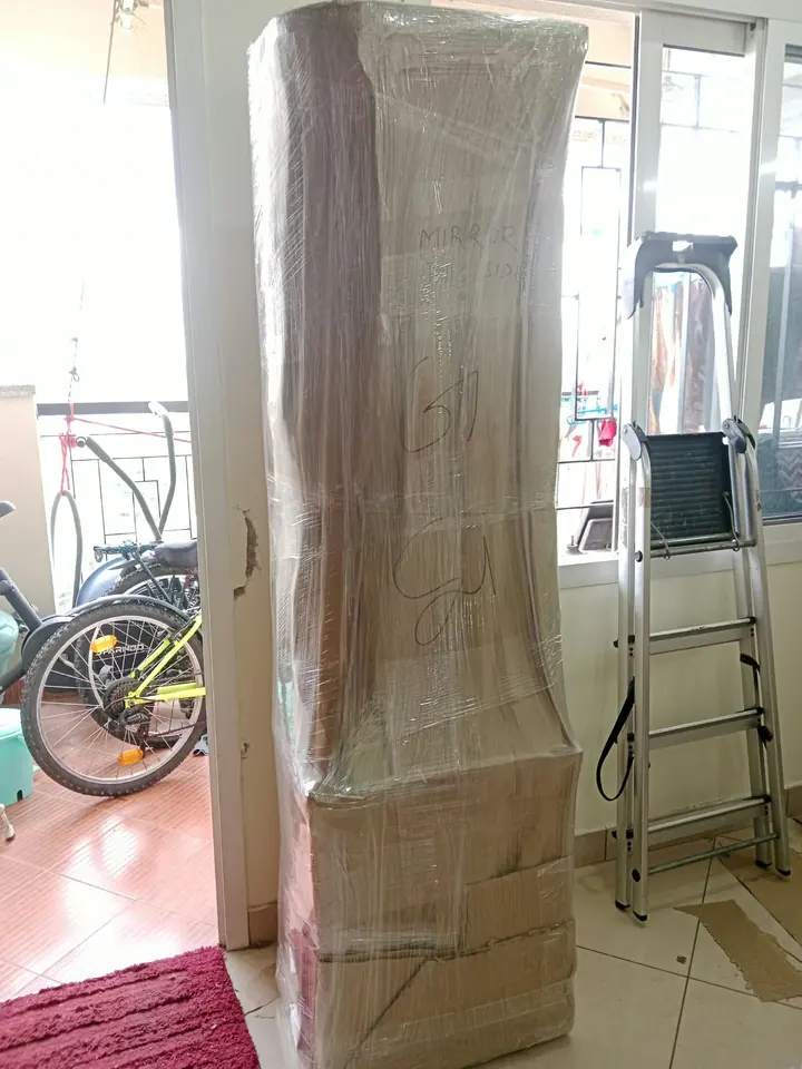 A tall rectangular furniture piece wrapped before removal from a room.