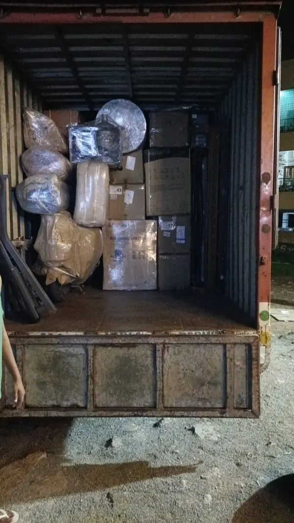 Wrapped household pieces, cartons and a round fan-like item grouped inside a goods vehicle.