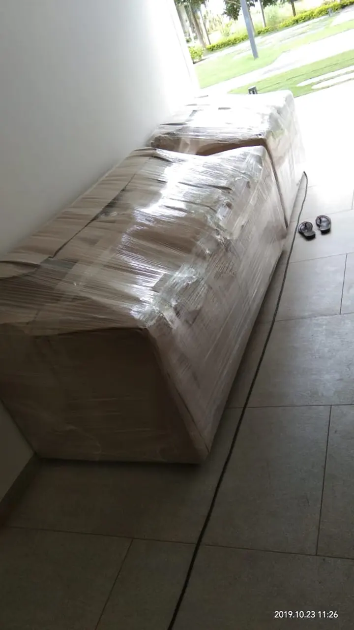A long sofa covered in protective wrapping beside a window inside a room.