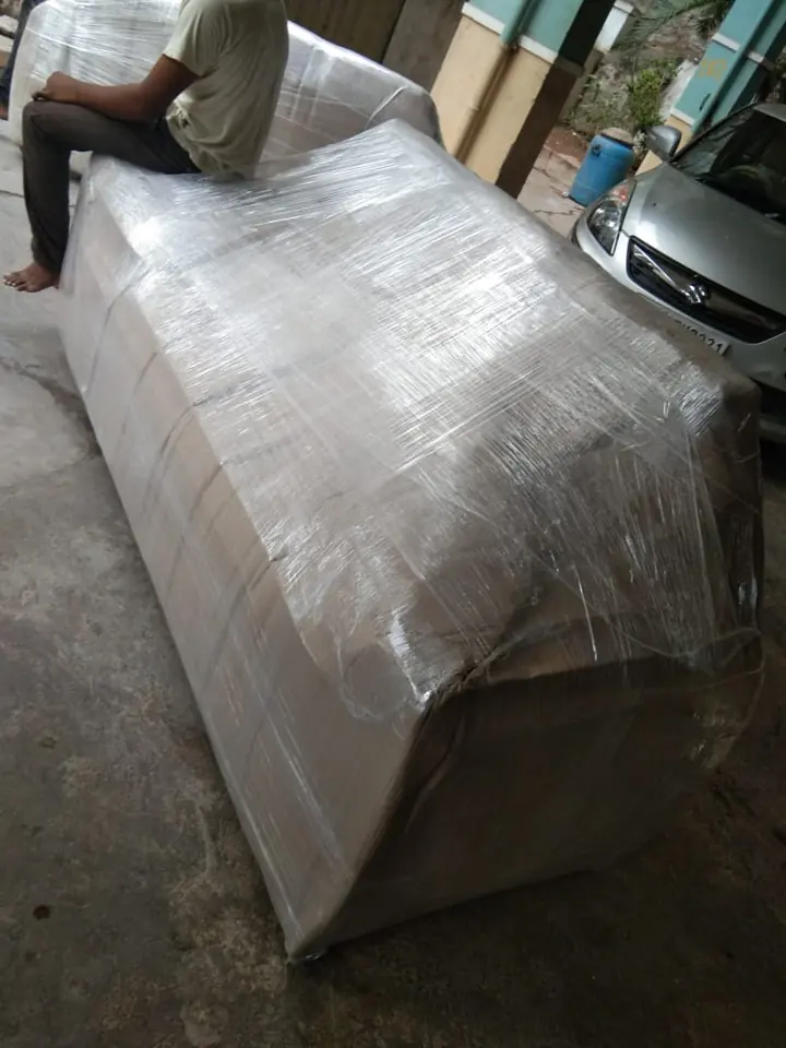 A person applying protective wrapping around a large sofa inside a home.