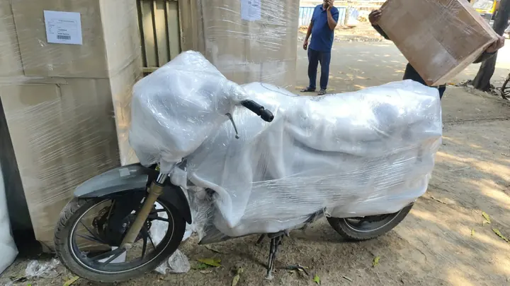 A motorcycle covered in protective wrapping beside packed household items outdoors.