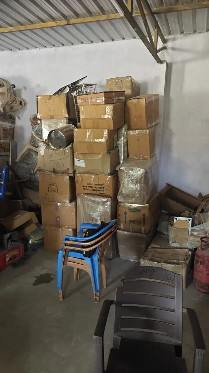 Cartons, wrapped belongings and plastic chairs grouped inside a storage area.