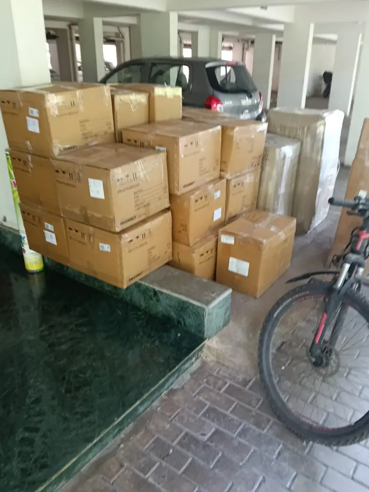 Stacked cartons and wrapped items with a bicycle in a building pickup area.