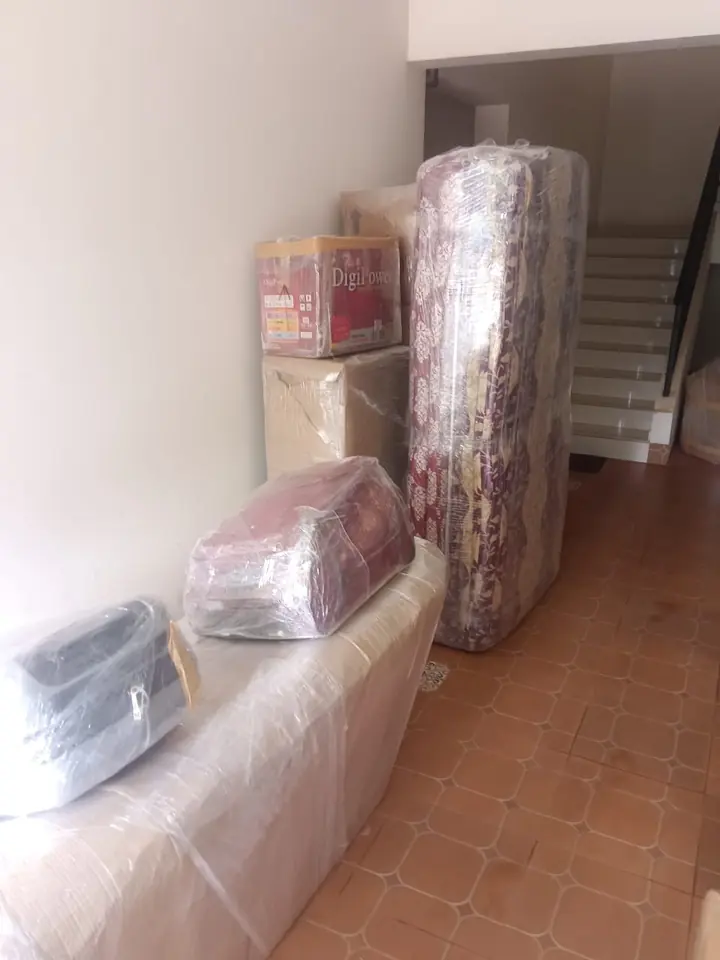 A wrapped sofa and other covered household pieces arranged indoors.