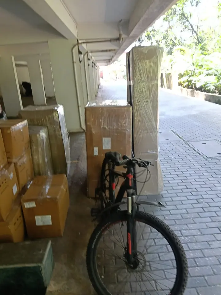 A bicycle beside sealed cartons and wrapped household items in a covered building area.