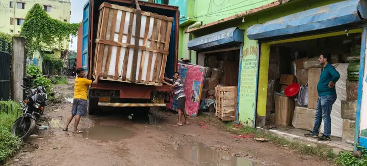 A cargo truck standing on a narrow street beside shopfronts, with its rear open.