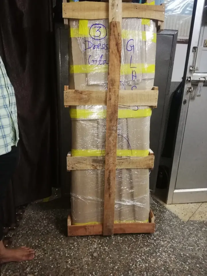A tall wooden-framed package secured with coloured straps near an entrance.