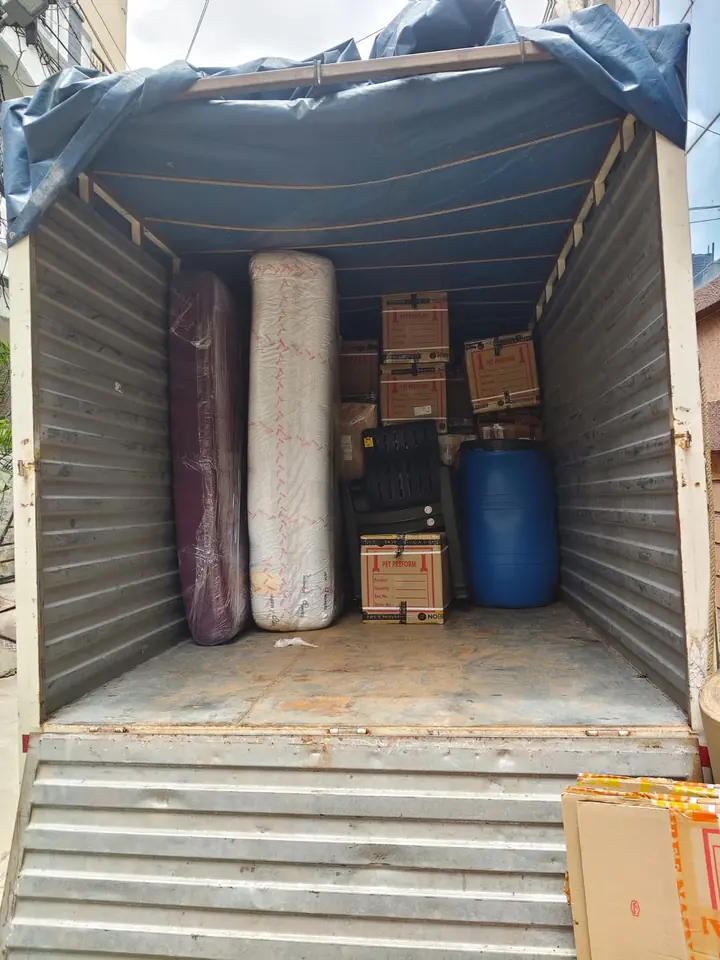 An enclosed goods vehicle containing tall wrapped items, cartons and a blue drum-shaped container.