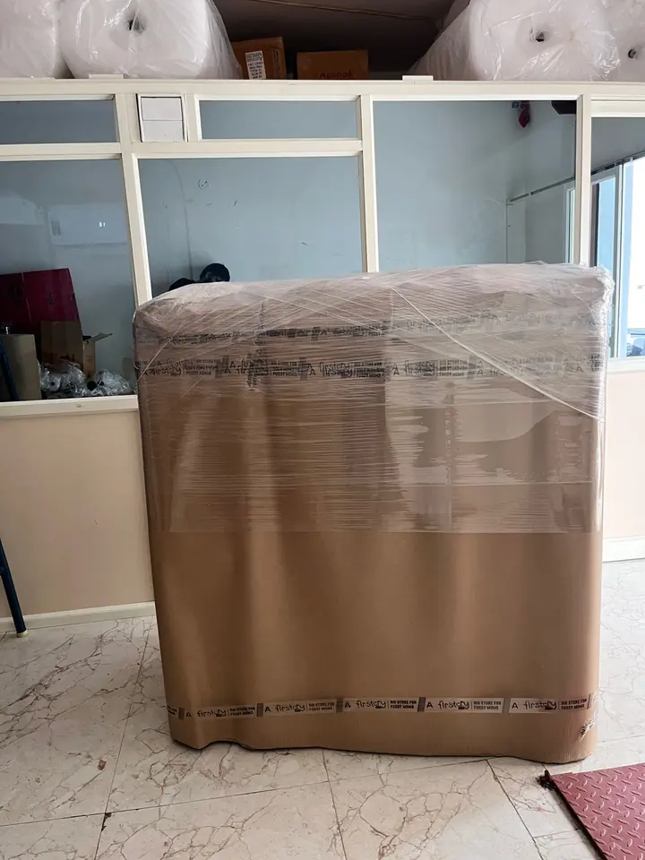 A broad furniture piece wrapped in cardboard and clear film inside a furnished room.