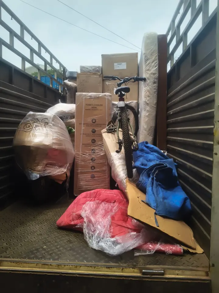 A bicycle standing among wrapped household packages inside an open-sided goods vehicle.