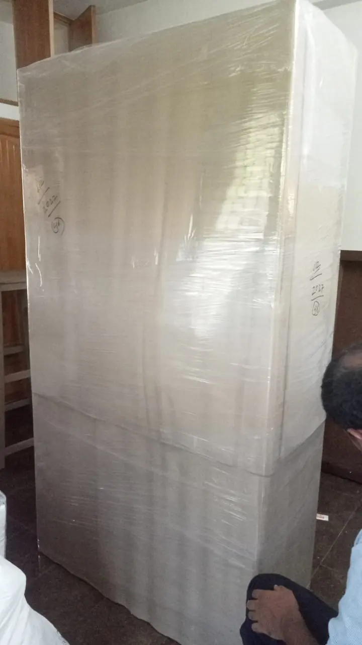 A large mattress standing inside a room with its surfaces covered in protective wrap.