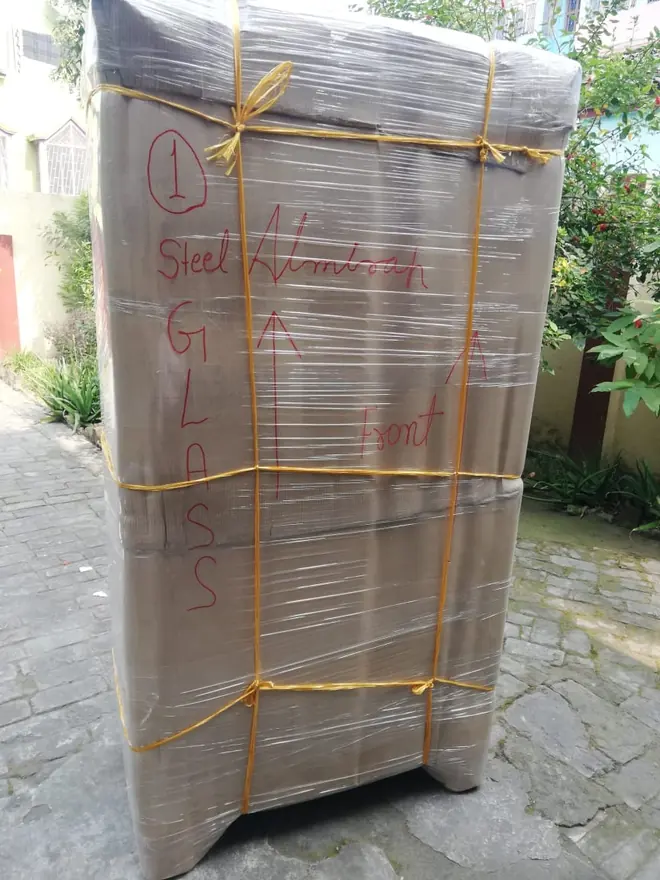 A tall wrapped cabinet-like item standing outdoors, secured with cord around its covering.