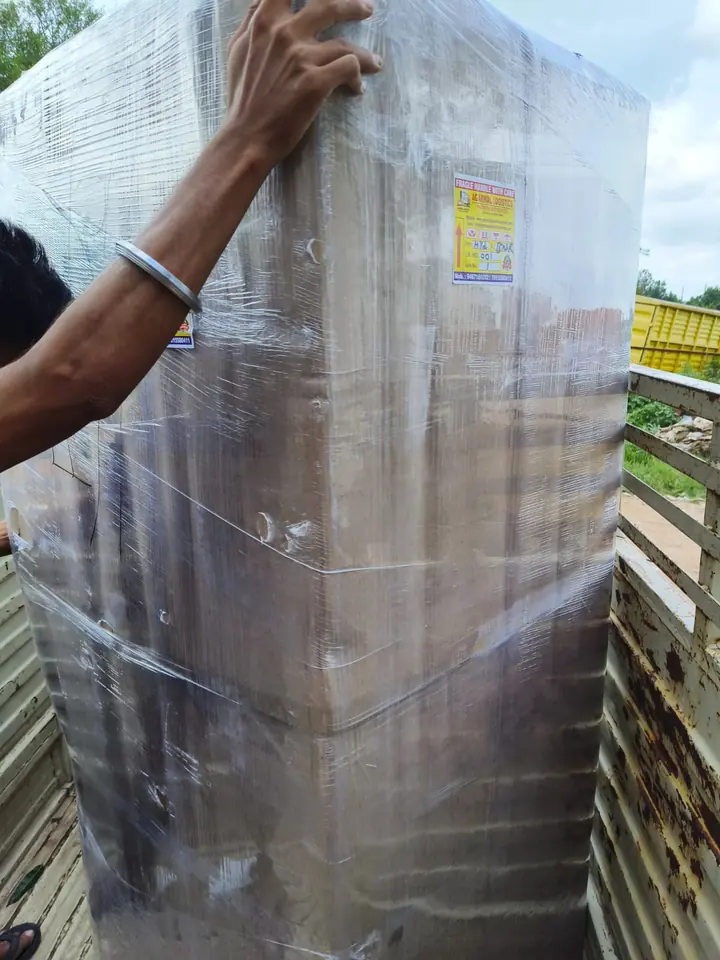 A tall appliance covered in protective wrapping, with a person beside it outdoors.