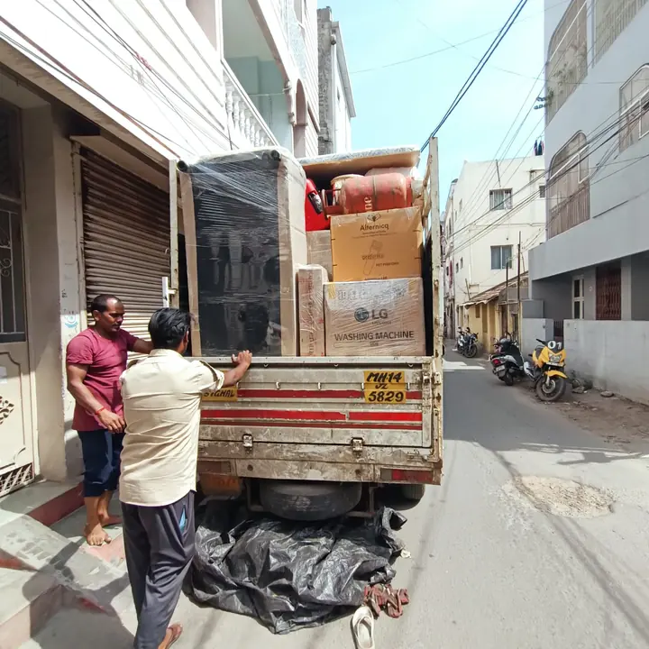 People beside a small goods vehicle loaded with household items outside a building.