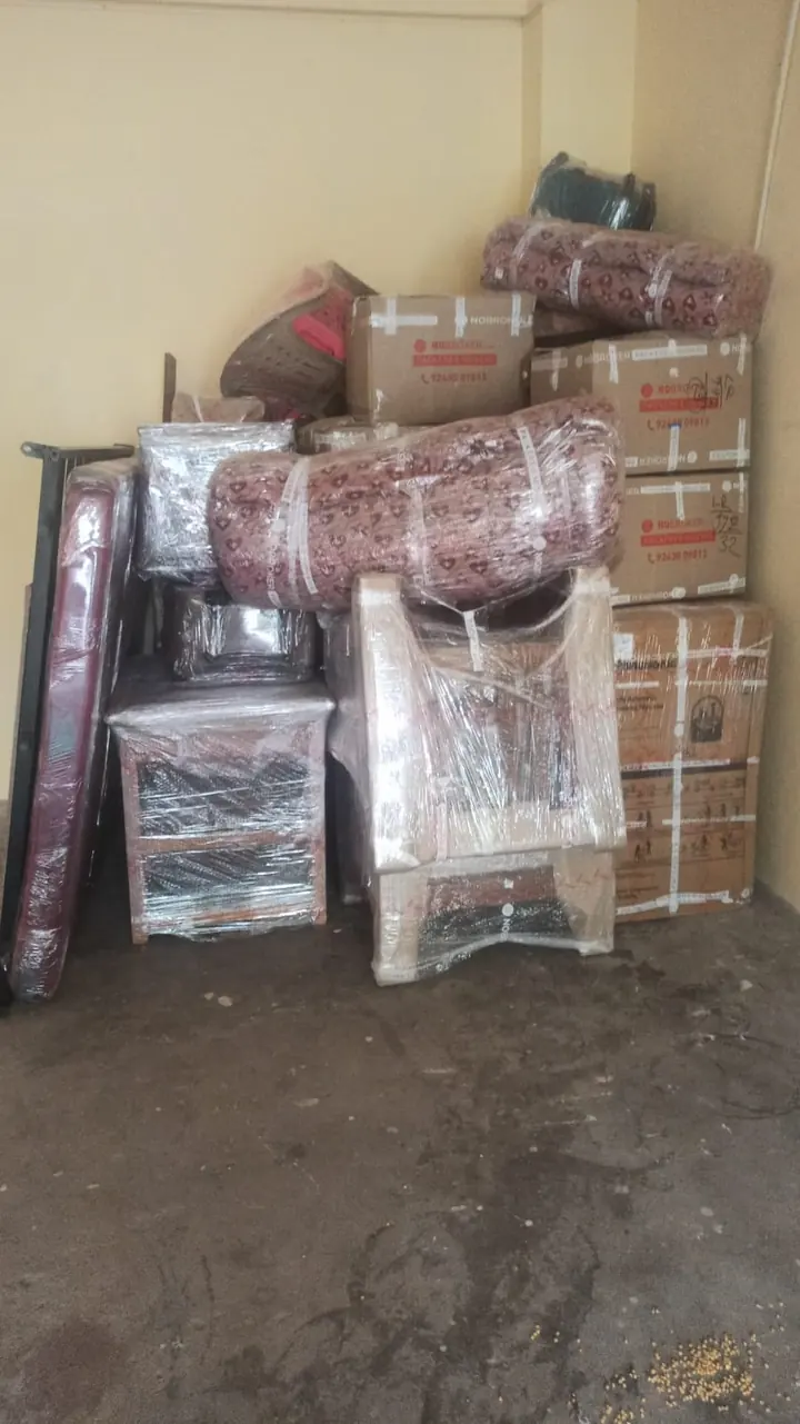 Wrapped furniture pieces and cartons grouped against a wall in a storage area.