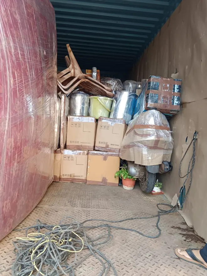 A mixed load of cartons, chairs and other household pieces inside a cargo vehicle.