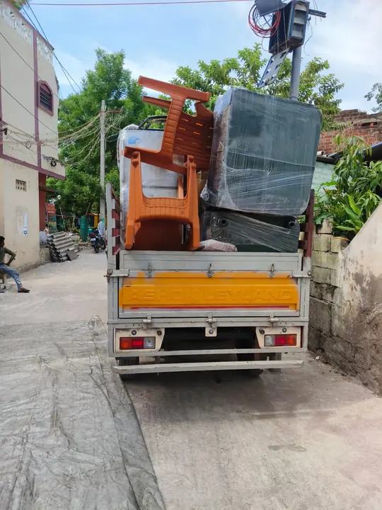 A small loaded goods vehicle standing outdoors with tall household items at its rear.