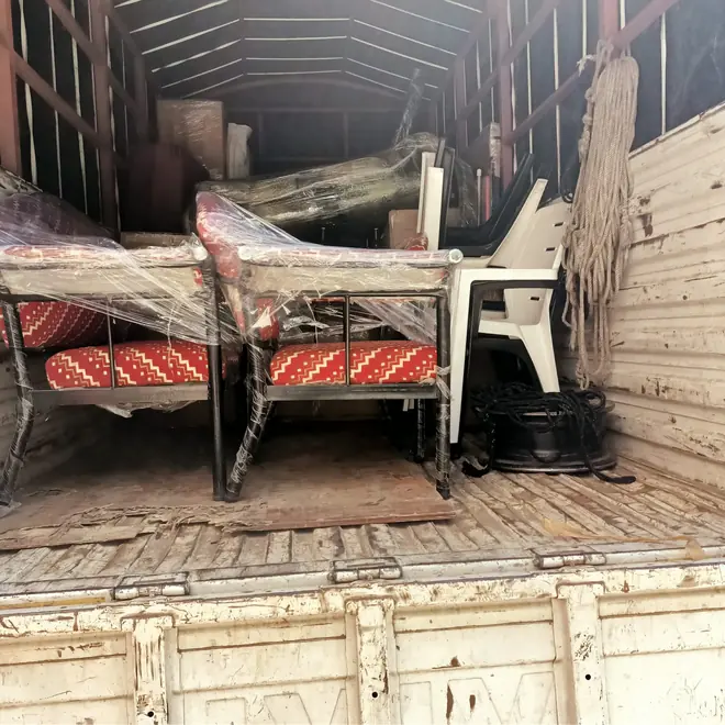 Chairs and other furniture arranged inside a goods vehicle, with protective material around parts of the pieces.