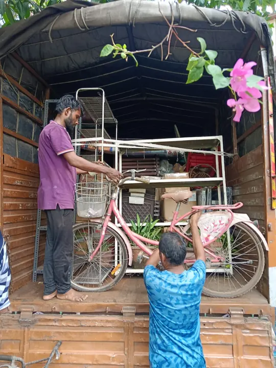 People handling a bicycle at the open rear of a goods vehicle containing household items.